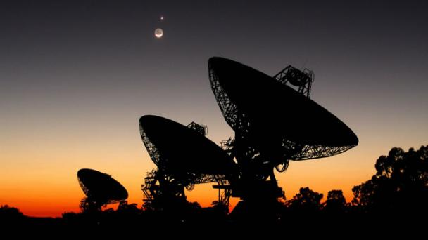 Radio telescope array pointed at sky with sunset behind